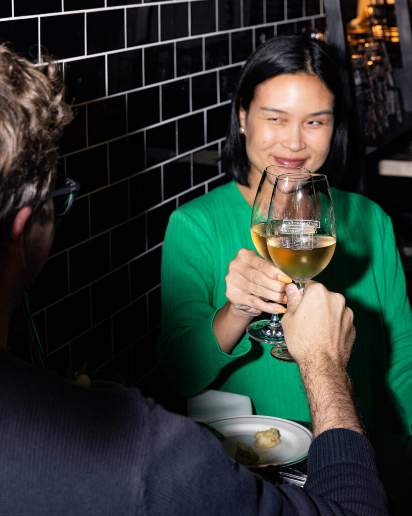 A woman in a green shirt smiles as she clinks her glass with her date.